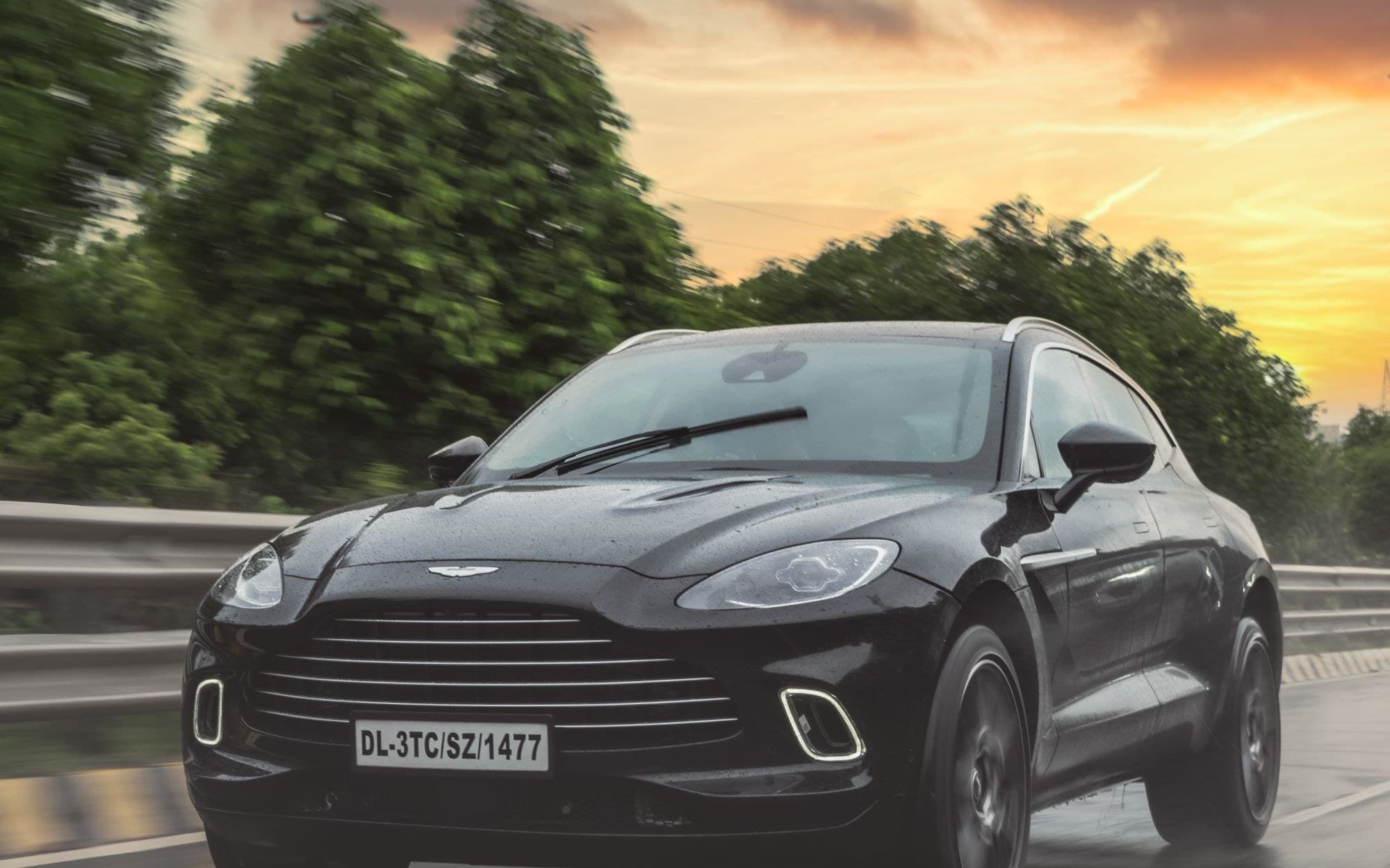 Black Aston Martin DBX driving on a wet highway at sunset