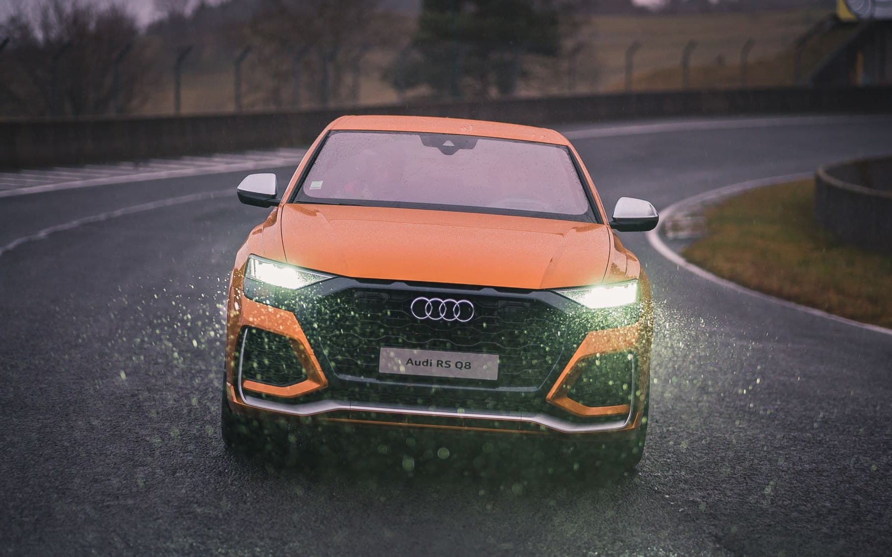 Orange Audi RS Q8 performance SUV on a wet racetrack in the rain