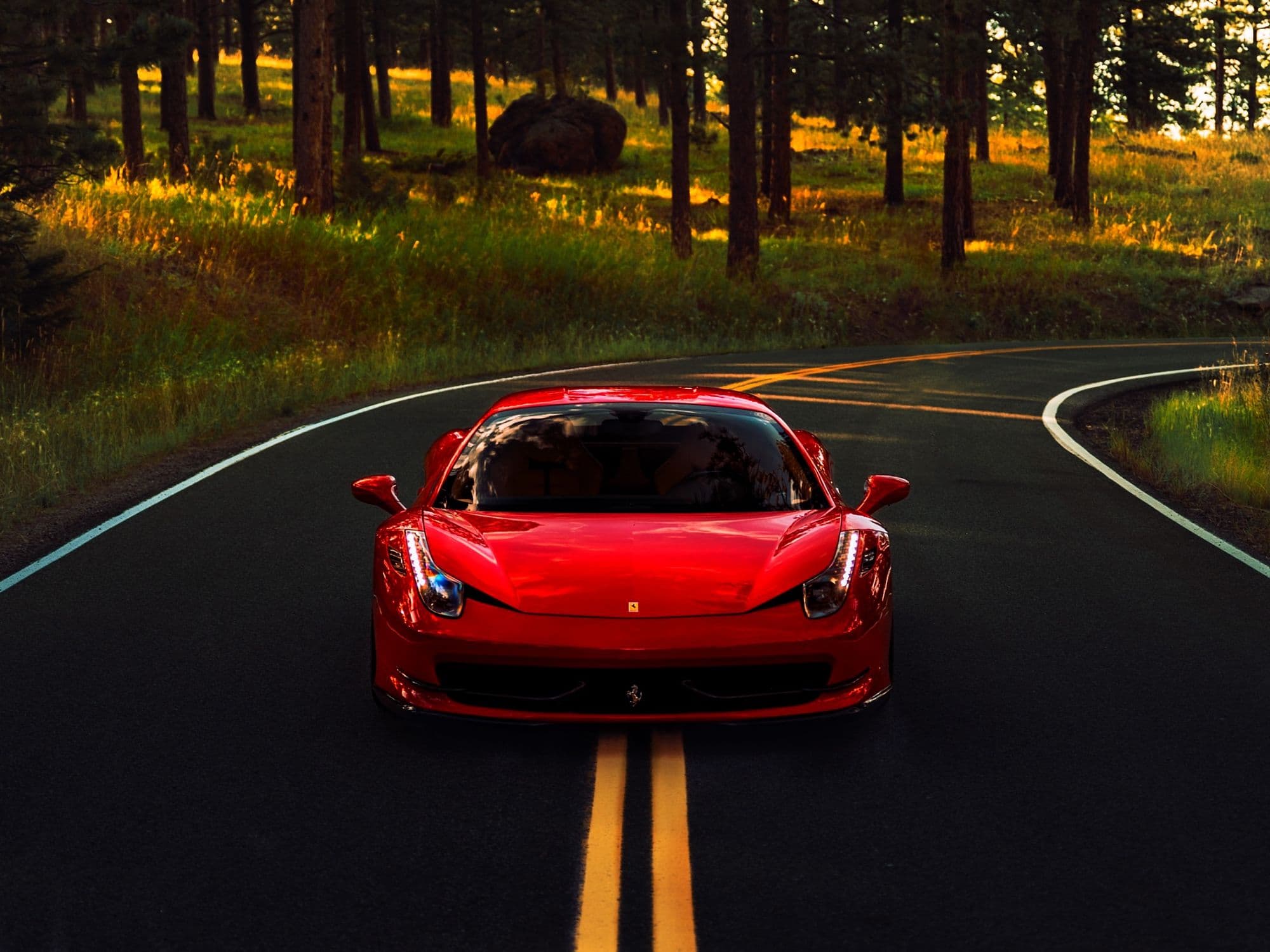 Red Ferrari 458 Italia on a winding forest road at golden hour