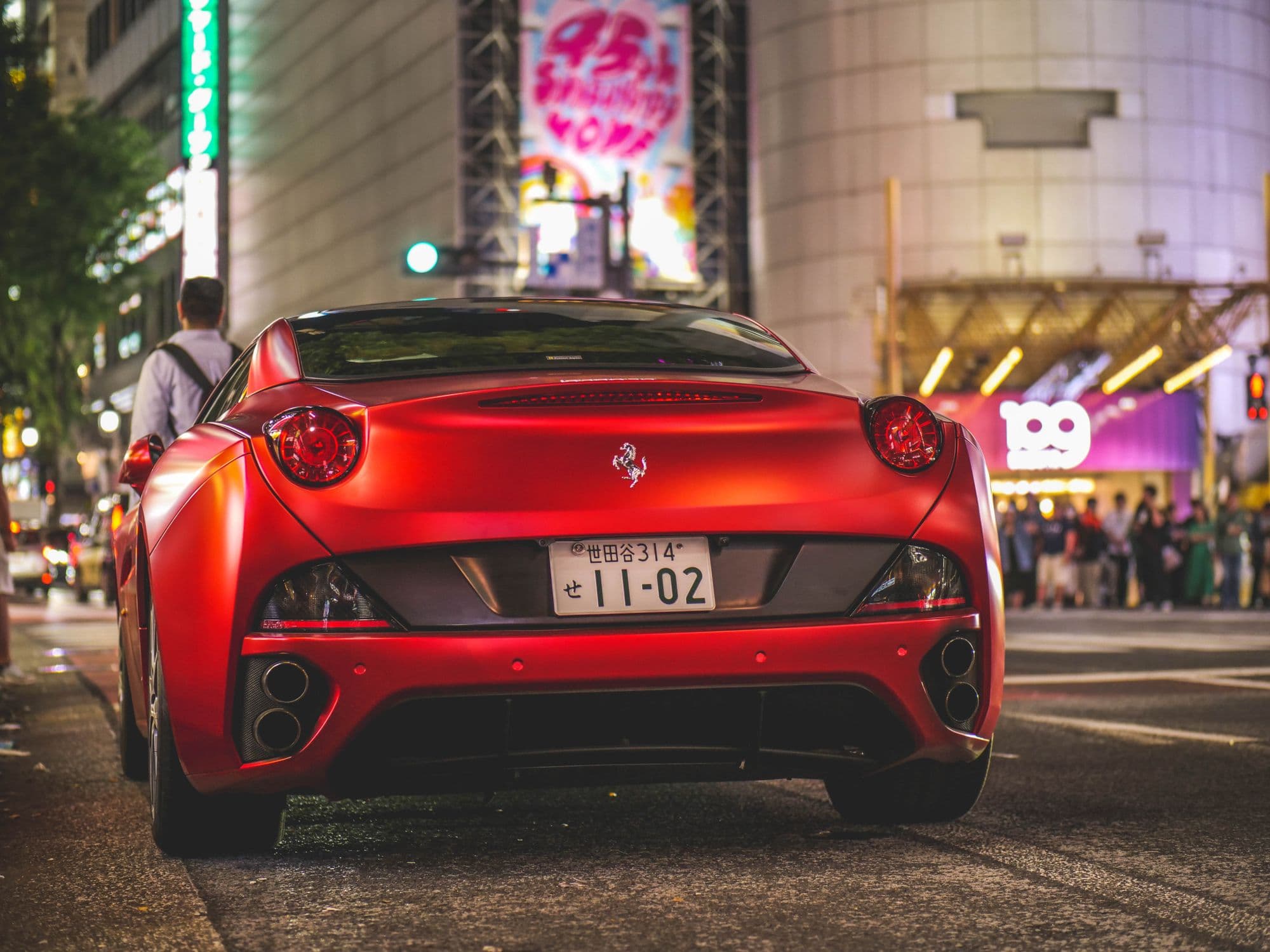 Red Ferrari California driving through a neon-lit city street at night