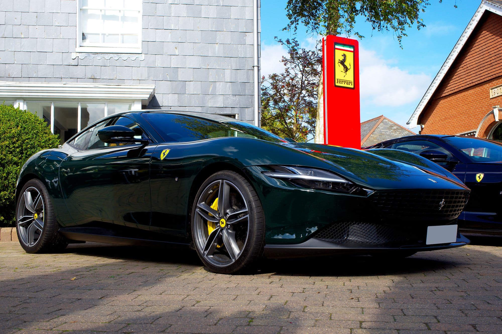 Dark green Ferrari Roma parked in front of a Ferrari dealership