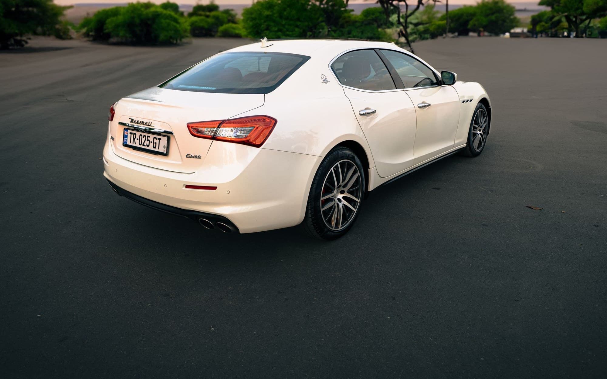 White Maserati Ghibli sedan parked under a dramatic evening sky