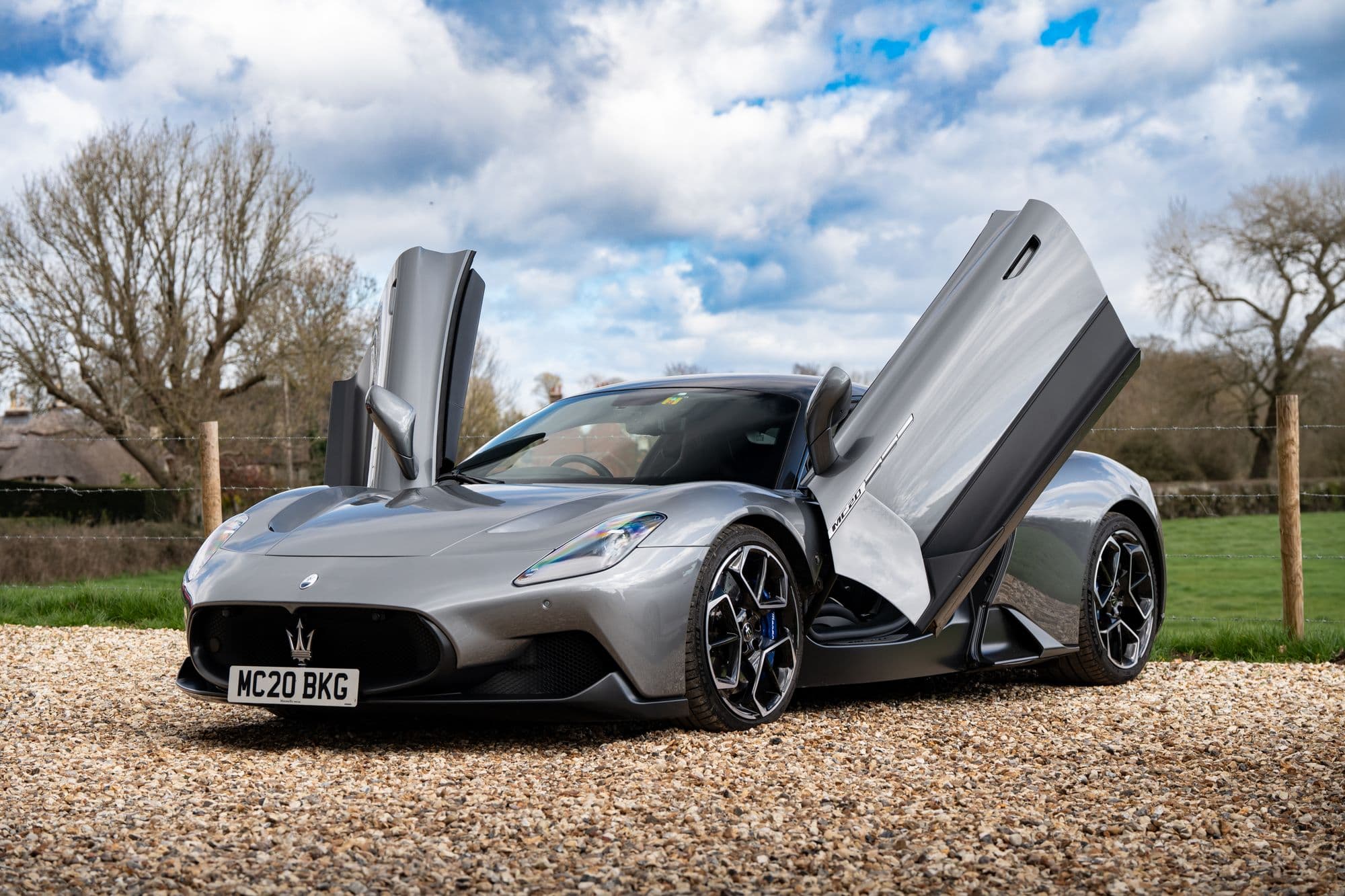 Silver Maserati MC20 with its butterfly doors open in the countryside
