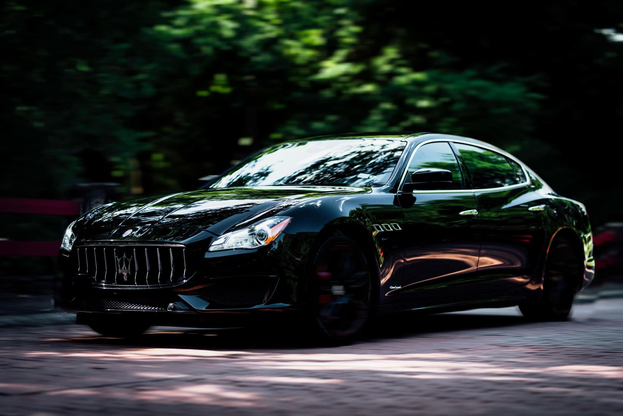 Black Maserati Quattroporte driving on a shaded tree-lined road