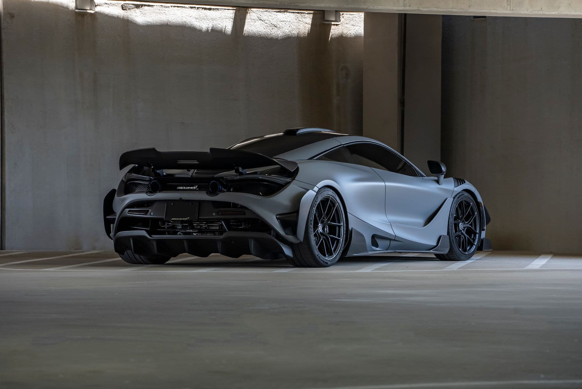 Gray McLaren supercar with a large rear wing parked in a concrete garage