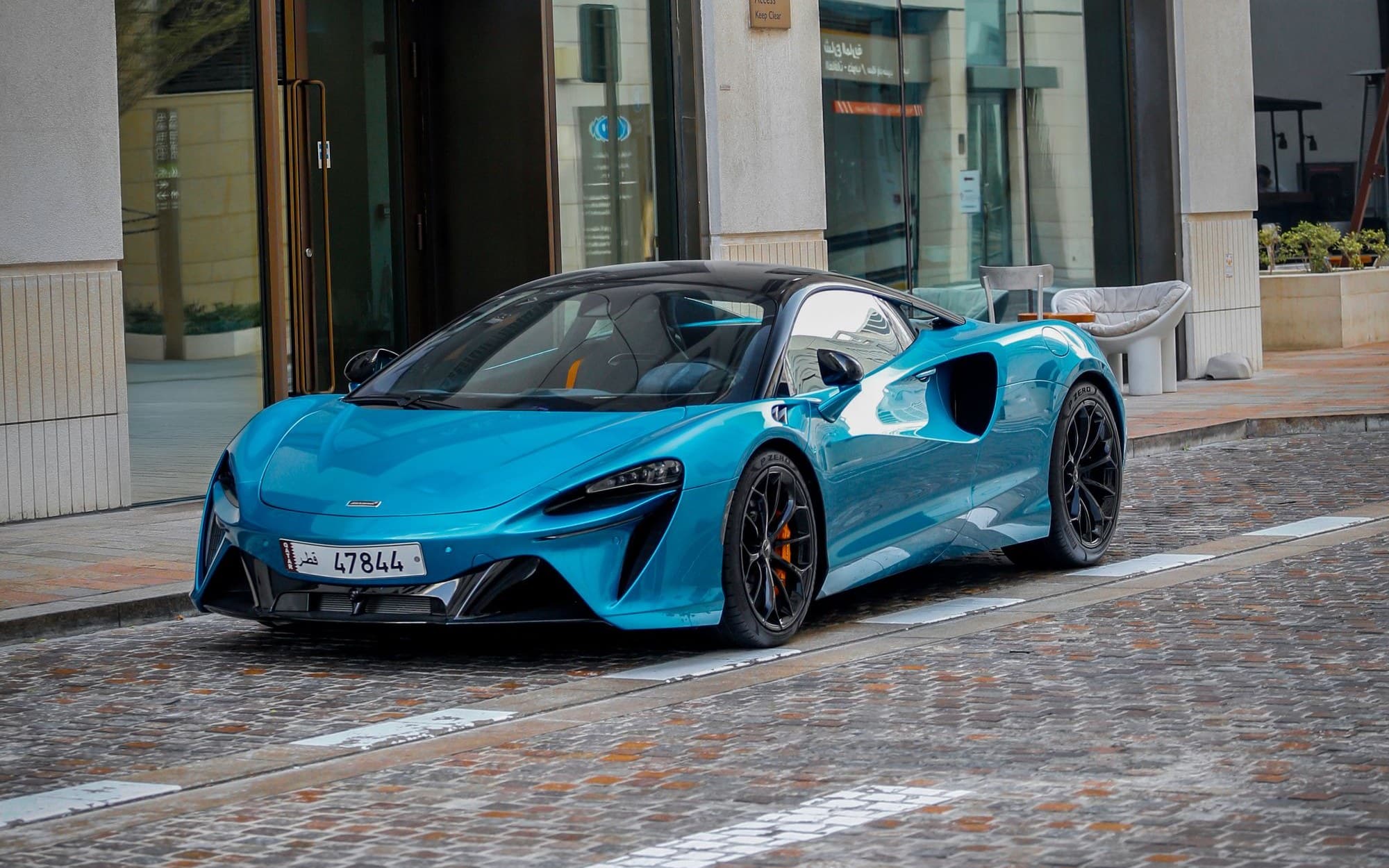 Blue McLaren Artura parked on a cobblestone street outside a restaurant