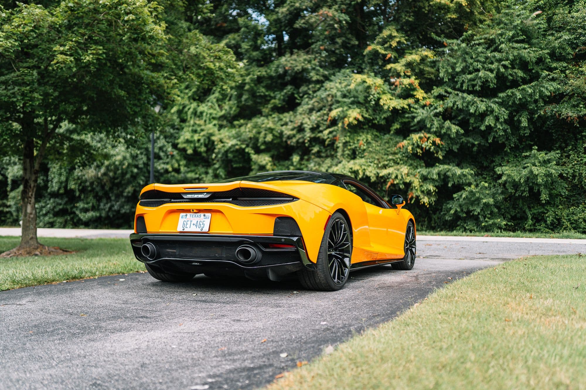 Rear view of a yellow McLaren GT parked on a tree-lined driveway