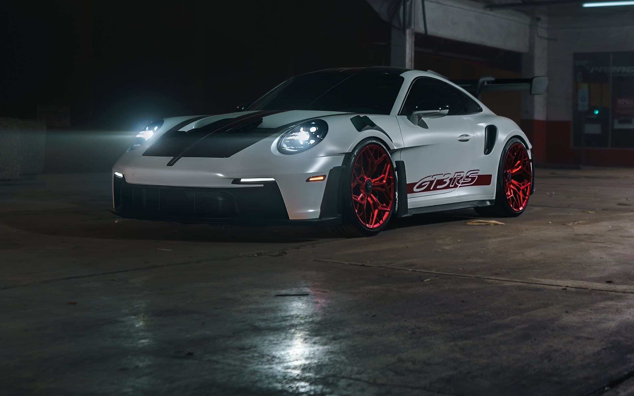 White Porsche 911 GT3 RS with red wheels in a dark workshop
