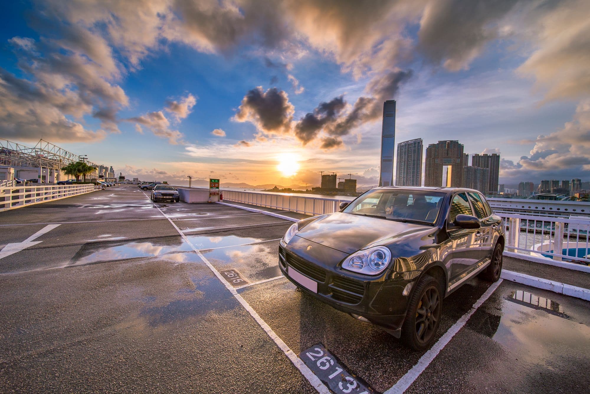Black Porsche Cayenne on a rooftop parking lot at sunset with a city skyline behind