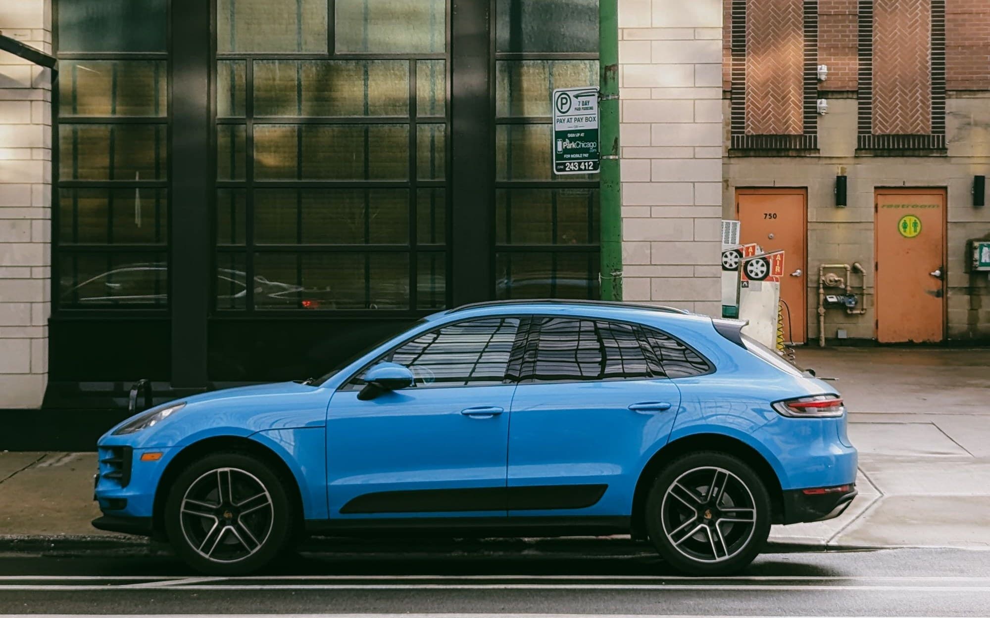 Blue Porsche Macan parked on a city street beside a brick building