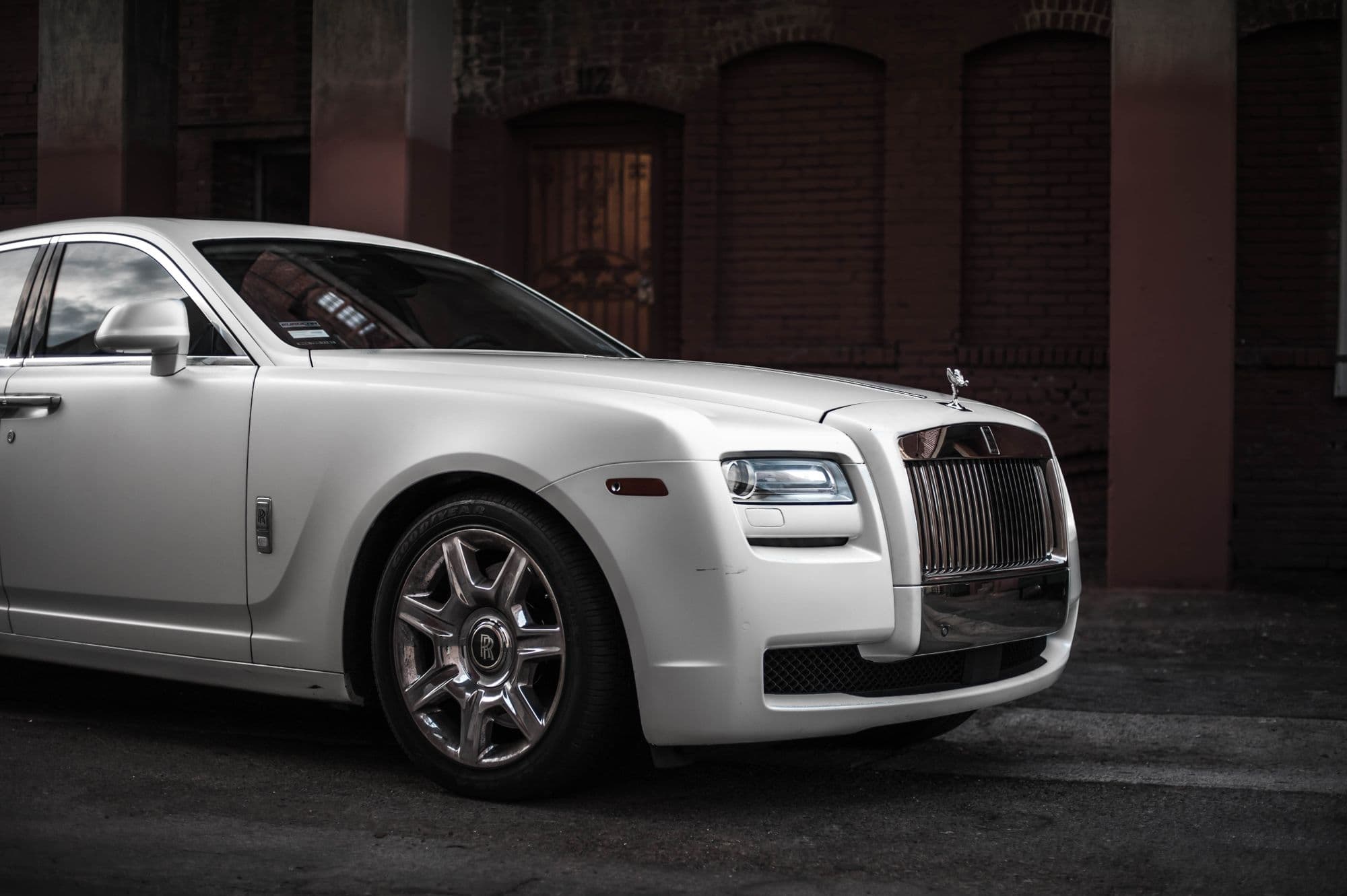 White Rolls-Royce Ghost parked beside a dark brick building